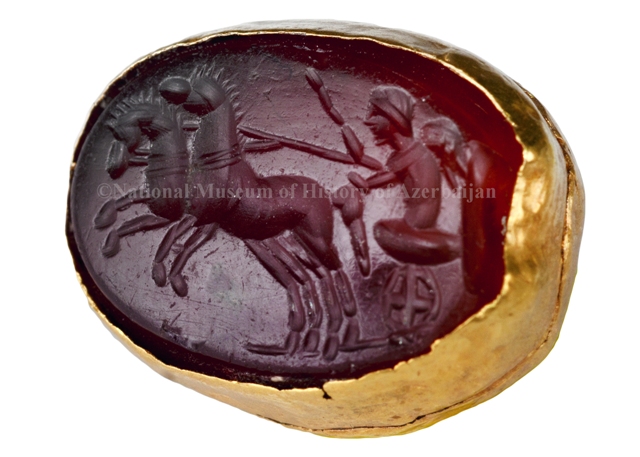 Tarix Muzeyində üzərində insan və cəng arabası təsvir olunan arxeoloji qızıl çərçivəli möhür qorunur